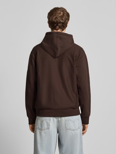 Männermodel trägt Hoodie mit Kapuze von Carhartt Work In Progress in Braun aus Baumwoll-Mix, Lockerer-Schnitt, Ganzkörperansicht Rückansicht.