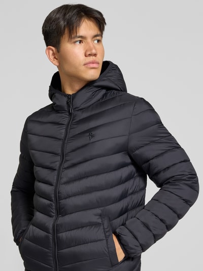 Männermodel trägt Steppjacke mit Kapuze und Label-Stitching von REVIEW in Schwarz, horizontale Steppnähte, Regular Fit, Nahaufnahme Oberkörper. Rückenlänge 69 cm, Schulterbreite 47 cm, Brustweite 53 cm, Ärmellänge 67 cm.