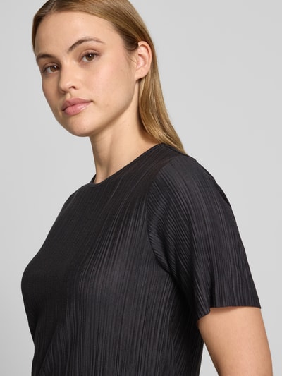 Frauenmodel trägt T-Shirt mit Rundhalsausschnitt Modell 'LISA' von Vila, schwarzer Material-Mix mit Viskose-Anteil, Plisseefalten, Nahaufnahme Oberkörper.