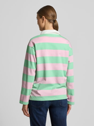 Frauenmodel trägt Regular Fit Poloshirt aus reiner Baumwolle von s.Oliver RED LABEL, gestreift in Rosa und Grün, Piqué-Material, Ganzkörperansicht Rückansicht.