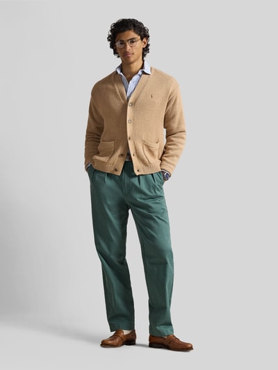 Męski model nosi Regular Fit Strickjacke aus reiner Baumwolle od Polo Ralph Lauren w kolorze beżowym, gładka faktura, krój regular fit, zapięcie na guziki, haftowane logo, długi rękaw, prążkowane wykończenia, kieszenie naszywane, materiał bawełniany, pełny widok z przodu.