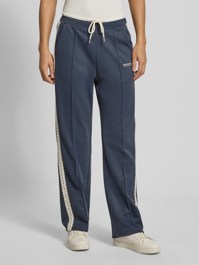 Kobiece modelka nosi spodnie typu track pants z mieszanki bawełny, model 'TIHANY LACE' od Pegador, obszycie koronką, wyhaftowane logo, krój regular fit, elastyczny pas, długość wewnętrzna nogawki w rozmiarze S: 77 cm, widok całej sylwetki z przodu