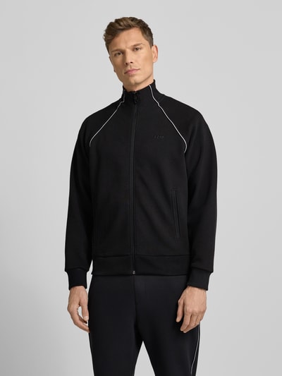 Männermodel draagt Regular Fit Sweat-Anzug aus Baumwoll-Mix Modell 'TRACKSUIT SET' van BOSS Green in effen zwart, piquétextuur, met ritssluiting, tunnelkoord, label-stitching en galonstrepen, zijzakken, ribboorden. Ganzkörperansicht von vorne.