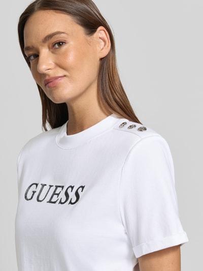 Vrouwenmodel draagt Cropped T-shirt met logo model 'MARINA' van Guess, puur katoen, korte look, ronde hals, logoprint, ruglengte bij maat S 45 cm, detailopname bovenlichaam.