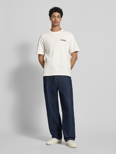 Męski model nosi Regular Fit T-Shirt mit Motiv-Print Modell 'DRY RIDGE' od Dickies z bawełny, okrągły dekolt, długość tyłu w rozmiarze M: 66 cm, cała sylwetka z przodu.