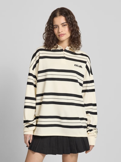 Kobiece model prezentuje Oversized Polo-Langarmshirt mit Streifenmuster von Karo Kauer, mieszanka bawełny, wyhaftowane logo, listwa guzikowa, krój oversized, wzór w paski, długość tyłu w rozmiarze S: 71 cm, jasny z czarnymi paskami, faktura gładka, całkowity widok z przodu