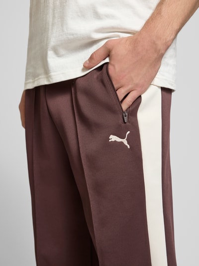 Männermodel trägt Straight Fit Sweatpants mit Logo-Stitching Modell 'Always On' von PUMA PERFORMANCE in Braun mit weißen Streifen, Baumwoll-Mix, elastischem Bund, Ziernähte und Reißverschlusstaschen, Nahaufnahme Oberkörper