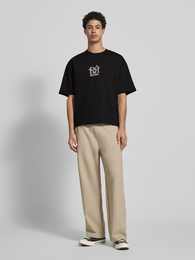 Mężczyzna model nosi Oversized Fit T-Shirt mit Logo-Stitching od REVIEW, czarna bawełna, florystyczne przeszycia, okrągły dekolt, długość tyłu 70 cm w rozm. M, pełny widok z przodu