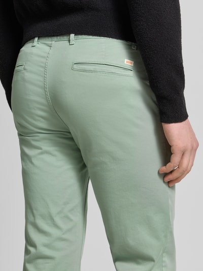 Männermodel trägt Slim Fit Chino aus Baumwoll-Mix Modell 'Chino Slim' von BOSS Orange in Hellgrün, Twill-Struktur, Nahaufnahme Rückansicht.