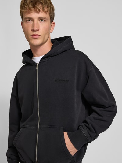 Männermodel trägt Regular Fit Sweatjacke aus Baumwoll-Mix von PEGADOR in Schwarz mit Logo-Stickerei, geteilte Kängurutasche, durchgehender Zipper, gerippte Abschlüsse, Langarm, Nahaufnahme Oberkörper.