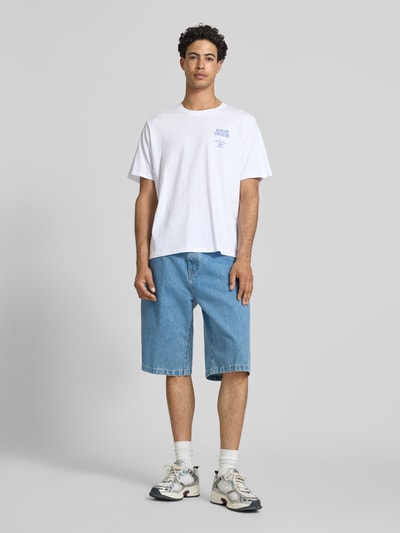 Männermodel trägt Herren T-Shirt von Jack & Jones aus Reine Baumwolle, Relaxed-Fit, Modell 'Photo', Statement-Print, Rundhalsausschnitt, Rückenlänge bei Größe M 70 cm, weiß mit blauem Print, dazu blaue Jeansshorts, Ganzkörperansicht von vorne.