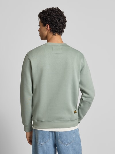 Męski model nosi bluzę z mieszanki bawełny Premium core od G-Star Raw, prosty krój, okrągły dekolt, wyhaftowane logo, długość tyłu 66 cm, długość rękawa 67 cm, elastyczne wykończenia, widok całej sylwetki od tyłu.