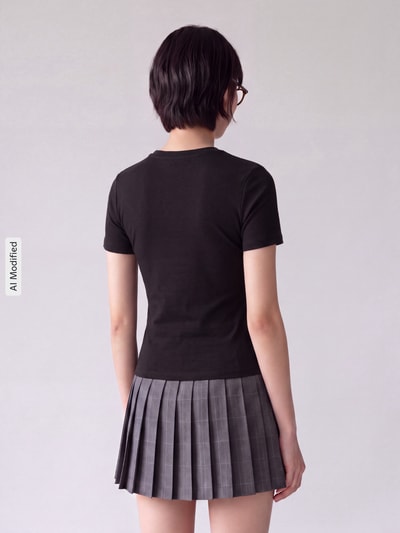 Frauenmodel trägt Slim Fit T-Shirt aus Baumwoll-Mix Modell 'RILEY' von ONLY, schwarz, kombiniert mit grauem Faltenrock, Ganzkörperansicht Rückansicht, Damen T-Shirt von ONLY, KI-modifiziertes Bild.