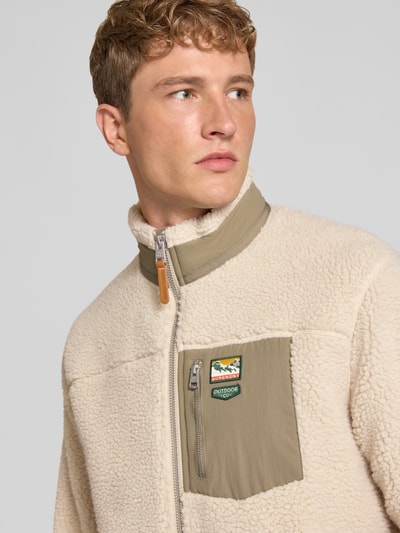 Männermodel trägt Fleecejacke mit Label-Details Modell 'MOUNTAIN' von Superdry in Beige mit Reißverschluss und Stehkragen, Nahaufnahme Oberkörper. Herren Fleecejacke aus Teddyfell, Regular Fit, Schulterbreite 50 cm, Brustweite 60 cm, Ärmellänge 66 cm, Rückenlänge 68 cm.