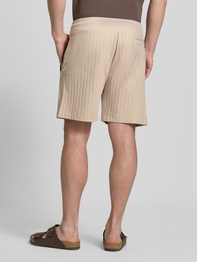 Männermodel trägt Regular Fit Shorts mit Tunnelzug Modell 'JUANITO' von JOOP! Collection aus beiger Baumwolle, Rückansicht, Ganzkörperansicht.