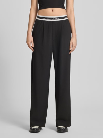 Modelka nosi spodnie Wide Leg Hose mit elastischem Logo-Bund od ANOTHER COTTON LAB, czarne, mieszanka materiałów z dodatkiem streczu, wpuszczane kieszenie, szerokość w rozmiarze S 36 cm, długość wewnętrzna nogawki 75 cm, widok od przodu, ujęcie całej sylwetki.