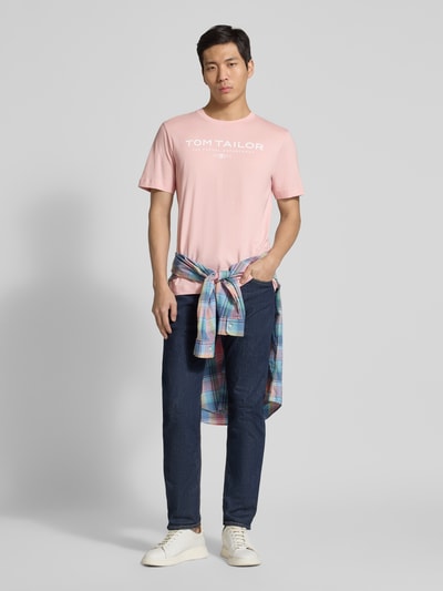 Männermodel trägt Regular Fit T-Shirt aus reiner Baumwolle von Tom Tailor in effen roze met labelprint, ronde hals, geheel van voren, ganzkörperansicht von vorne.