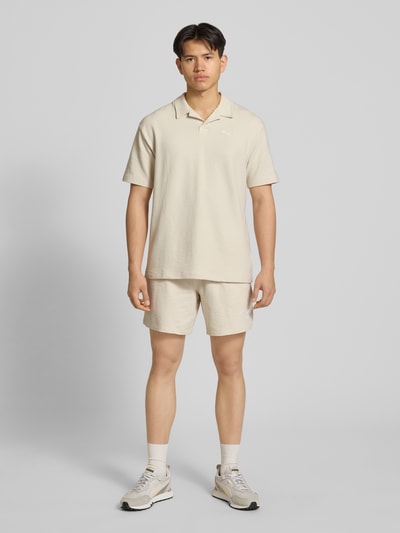 Männermodel trägt Regular Fit T-Shirt mit Logo-Stitching von PUMA PERFORMANCE in Beige, Strukturmuster, Reverskragen, Ganzkörperansicht von vorne.