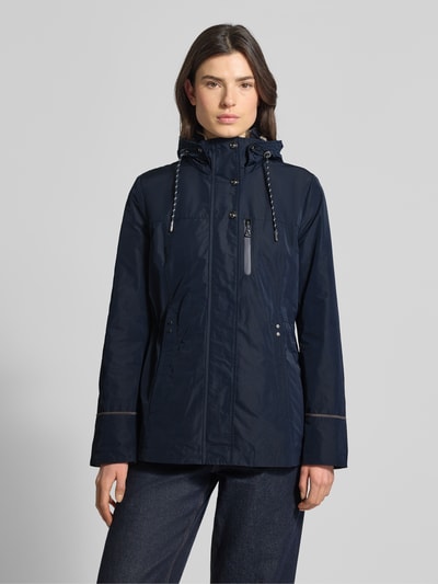 Frauenmodel trägt Funktionsjacke mit Brusttasche von Gil Bret in Dunkelblau, taillierte Passform, Kapuze, Stehkragen, Tunnelzug, Reißverschluss, glatte Struktur, Rückenlänge 74 cm, Schulterbreite 41 cm, Brustweite 47 cm, Ärmellänge 65 cm. Ganzkörperansicht von vorne.