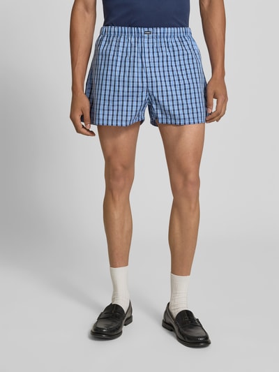 Männermodel trägt Boxershorts aus reiner Baumwolle von VETEMENTS mit Karo-Muster, lockerem Schnitt, elastischem Bund und Label-Patch, Ganzkörperansicht von vorne.