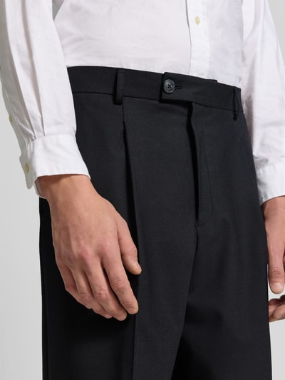 Männermodel trägt Straight Fit Stoffhose mit Bundfalten von ANNARR in Schwarz, glatte Textur, Nahaufnahme Oberkörper, Herrenmode-Kontext.