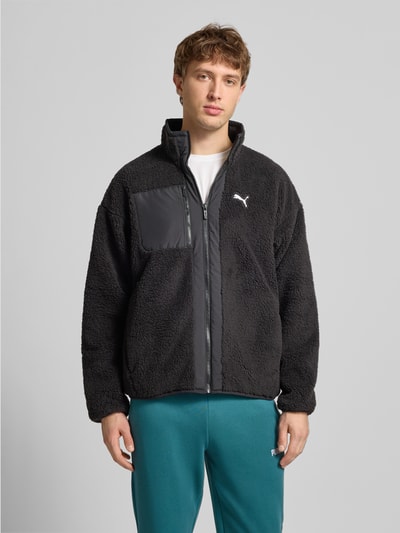 Męski model nosi Sherpa Jacket mit Reißverschluss od PUMA PERFORMANCE, czarny kolor, luźny krój, stójka, nadruk z logo, kieszenie zapinane na zamek błyskawiczny, długość tyłu 68 cm, szerokość ramion 60 cm, szerokość klatki piersiowej 63 cm, długość rękawów 59 cm, tekstura pluszowa, gładkie wstawki, całkowity widok z przodu