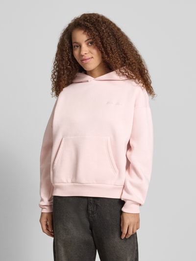 Vrouwenmodel draagt Hoodie met Logo-Print en Känguru-Tasche van REVIEW in lichtroze katoenmix, loose fit, capuchon, logoprint, kangoeroezak, schouderpartijen met dropped shoulders; vooraanzicht hele lichaam.