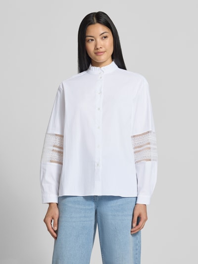 Frauenmodel trägt Regular Fit Bluse aus Baumwoll-Mix Modell 'Gala' von MANGO, weiß, Stehkragen, Rüschen, Langarm, Loch-Stitching, Ganzkörperansicht von vorne.