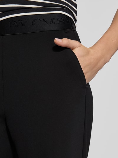 Frauenmodel trägt Stoffhose in verkürzter Passform Modell 'ELENA' von Cambio aus Material-Mix, elastischer Logo-Bund, Nahaufnahme Hüftbereich.