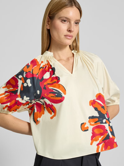 Frauenmodel trägt Regular Fit Bluse mit Tunikakragen und 1/2-Arm von HERZENS, bunte Blumenmuster auf cremefarbenem Baumwoll-Elasthan-Mix, Nahaufnahme Oberkörper. Rückenlänge 57 cm, Ärmellänge 41 cm bei Größe 36.