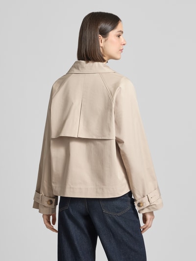 Kobiece modelka nosi Regular Fit Trenchcoat-Jacke aus Baumwoll-Mix Modell 'NEW CILO' od Selected Femme, jednokolorowy beżowy, kołnierz z połami, listwa guzikowa 2-rzędowa, kontrafałda z tyłu, raglanowe rękawy, mieszanka bawełny, widoczne kieszenie z wypustką, zakończenia rękawów z patkami, efekt: jednolity kolor, krój regular fit, widok całej sylwetki z tyłu.