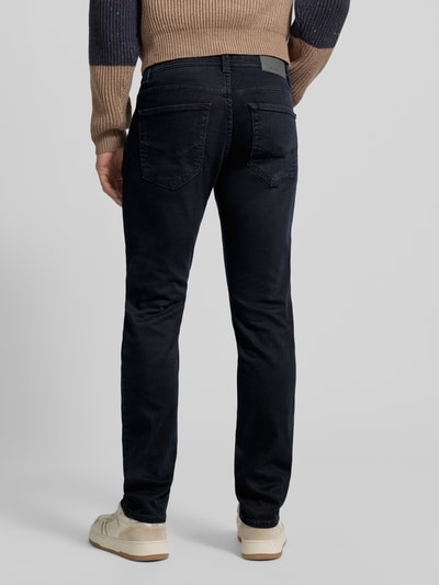 Mężczyzna nosi Tapered Fit Jeans mit Label-Detail Modell 'Lyon' von Pierre Cardin, mieszanka bawełny ze streczem, ciemnoniebieskie, detal z logo, szerokość w pasie 39 cm, długość wewnętrzna nogawki 79 cm, Ganzkörperansicht Rückansicht.