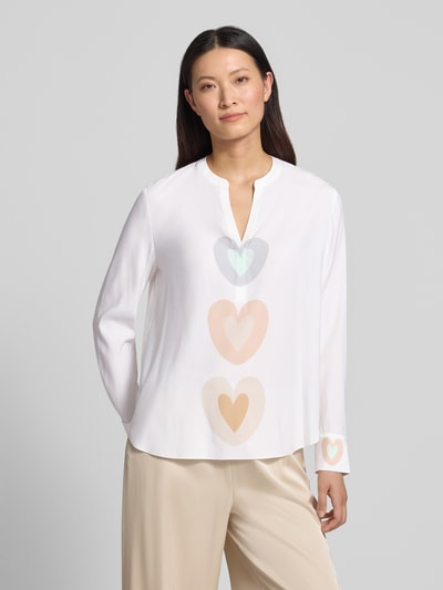 Kobiece modelka nosi Relaxed Fit Tunika-Bluse mit Allover-Motiv-Print von HERZENS, biała z nadrukiem serc, długie rękawy, dekolt z lamówką, tył przedłużony, długość tyłu w rozmiarze 36: 68 cm, długość rękawów: 63 cm, widok na cały przód.