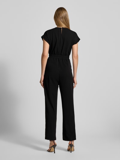 Frauenmodel trägt Jumpsuit mit Eingrifftaschen Modell 'Ko44a' von ZABAIONE, schwarzer Material-Mix mit Stretch-Anteil, Regular Fit, Ganzkörperansicht Rückansicht. Damen Jumpsuit, V-Ausschnitt, Rückenlänge bei Größe S 36 cm, Brustweite 41 cm, Ärmellänge 9 cm, Gesamtlänge 140 cm, Innenbeinlänge 70 cm.