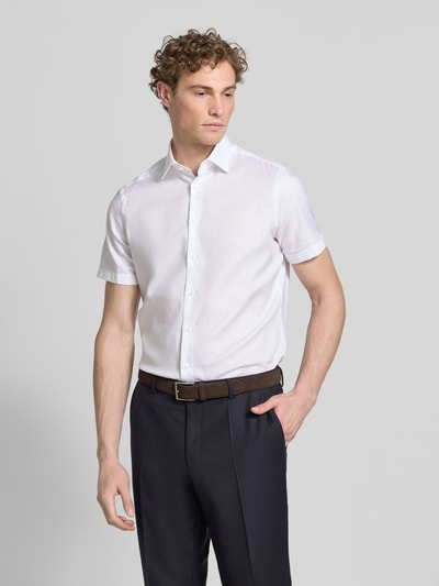 Męski model nosi Regular Fit Business-Hemd mit Kentkragen od Christian Berg Men, czysta bawełna, krój regular fit, biały, krótkie rękawy, guzik, długość tyłu w rozmiarze 39/40: 81 cm, szerokość w rozmiarze 39/40: 49 cm, długość rękawa w rozmiarze 39/40: 24 cm, ujęcie całej sylwetki z przodu.