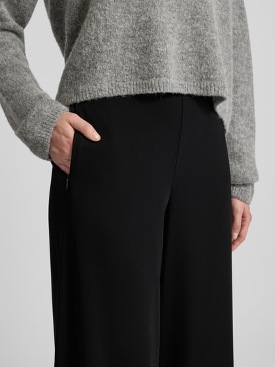 Frauenmodel trägt Wide Fit Stoffhose mit teilelastischem Bund Modell 'Coraline' von MAC, Schwarz, glatte Struktur, Nahaufnahme Oberkörper. Elastischer Material-Mix, Eingrifftaschen mit Reißverschluss, 38 cm Bundweite, 82 cm Innenbeinlänge, moderner Look.
