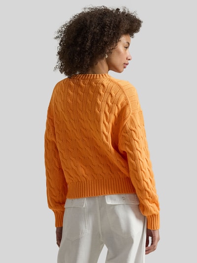 Vrouwenmodel draagt Regular Fit Strickpullover aus reiner Baumwolle van Polo Ralph Lauren, oranje kabelgebreid, logo-stiksel, katoen, lange mouw, geribde zoom, unicolor, crewneck, rugaanzicht.