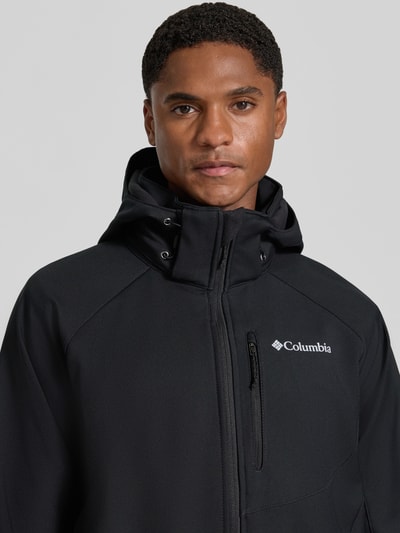Männermodel trägt Regular Fit Jacke mit Logo-Print Modell 'Cascade Ridge™' von Columbia in Schwarz, Softshell, Nahaufnahme Oberkörper.