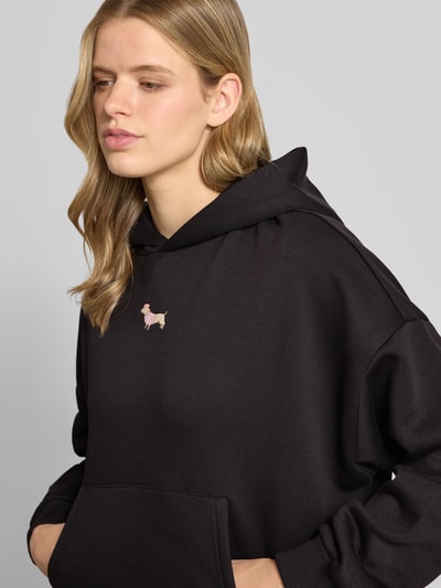 Frauenmodel trägt Hoodie mit Motiv-Stitching und Känguru-Tasche von REVIEW aus schwarzem Baumwoll-Mix, Regular-Fit, Nahaufnahme Oberkörper.
