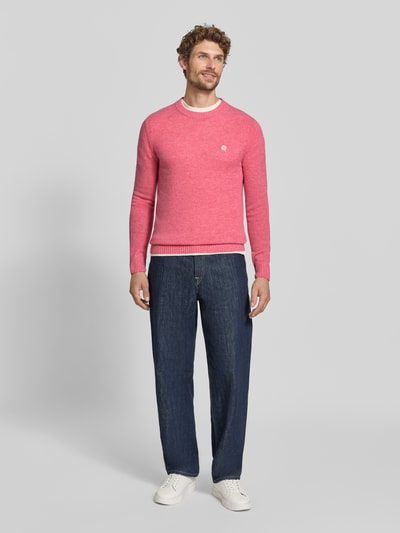 Männermodel trägt Slim Fit Strickpullover aus reiner Wolle mit Label-Stitching von MCNEAL, rosa, gerippte Abschlüsse, Ganzkörperansicht von vorne.