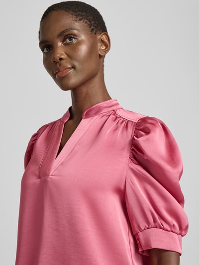 Kobieta nosi Blusenshirt mit Puffärmeln Modell 'Roella' od Neo Noir, satynowy materiał, serafino kołnierzyk, różowy kolor, zbliżenie na górną część ciała