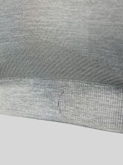 Frauenmodel trägt Triangel-BH mit Logo und gekreuzten Trägern von PUMA, grauer Material-Mix mit Stretch-Anteil, Logo, körpernahe Passform, Hakenverschluss, Nahaufnahme Oberkörper.