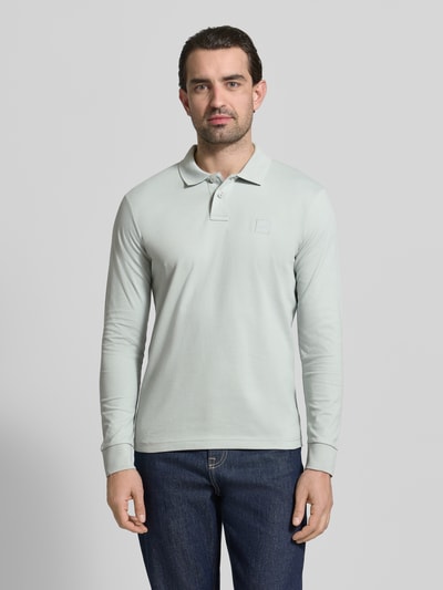 Männermodel trägt Slim Fit Poloshirt aus Baumwoll-Mix Modell 'PASSERBY' von BOSS Orange, unifarben, langarm, Ganzkörperansicht von vorne.