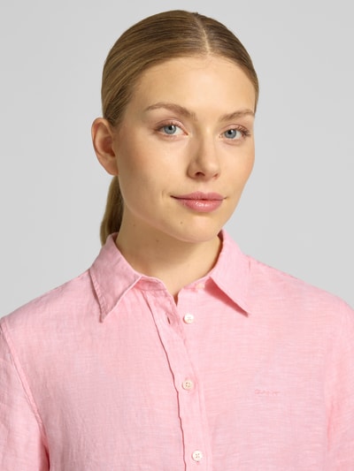 Kobiece modelka ma na sobie Regular Fit Leinenbluse mit Label-Stitching od Gant, różowy len, kołnierzyk koszulowy, listwa guzikowa, wyhaftowane logo, długość tyłu 66 cm, długość rękawów 60 cm, bluzka lniana, damska, zdjęcie zbliżenie górnej części ciała.