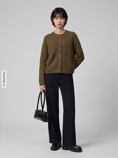 Kobiece model nosi kardigan rozpinany Relaxed Fit Strickjacke aus Woll-Mix mit Alpaka-Anteil model 'LULU' od Selected, oliwkowy, czarne spodnie, czarna torebka, kremowe tło, kontekst: damski kardigan rozpinany od Selected, pełen widok z przodu, obraz zmodyfikowany przez KI.
