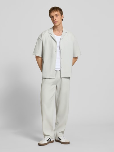 Männermodel trägt Relaxed Fit Freizeithemd mit Reverskragen Modell 'Troy' von Pegador, strukturierte Oberfläche, durchgehende Knopfleiste, hellgraue Farbe, Logostick, Kurzarm, Ganzkörperansicht von vorne.