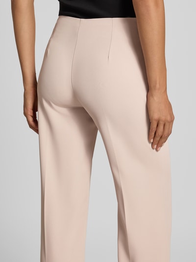 Vrouwenmodel draagt Flared Fit broek met bandplooien van Rinascimento, elastische materiaalmix, naadritssluiting, binnenbeenlengte maat S 85 cm, bandwijdte maat S 37 cm, kleur lichtbeige, gladde stof, Ganzkörperansicht Rückansicht.