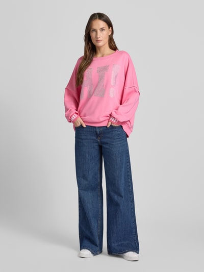 Modelka kobieca nosi różowy Sweatshirt mit Label-Detail od miss goodlife z bawełny, luźny krój, okrągły dekolt, dżersej, widok z przodu cała sylwetka.