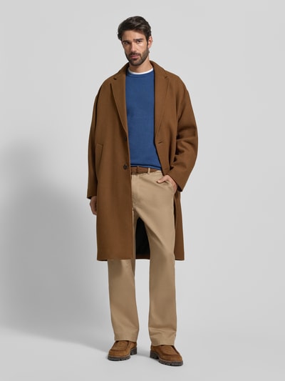 Mannelijk model draagt Regular Fit Strickpullover aus reiner Baumwolle van Tommy Hilfiger, unie kleur blauw, structuur, logo-detail, ronde hals, lange mouw, geribde boorden, piqué katoen, boven beige chino en bruine jas, volledige lichaamsvoorzijde.