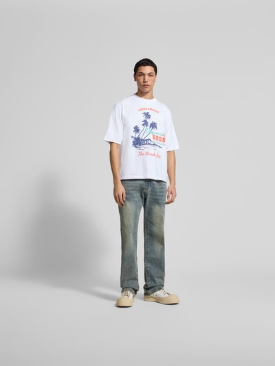 Männermodel trägt Loose Fit T-Shirt aus reiner Baumwolle von Dsquared2, weiß mit Motiv-Print und Label-Details, Ganzkörperansicht von vorne.